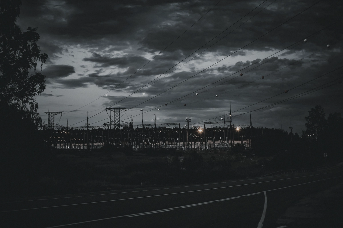 An electrical substation at dusk under a heavy overcast sky.