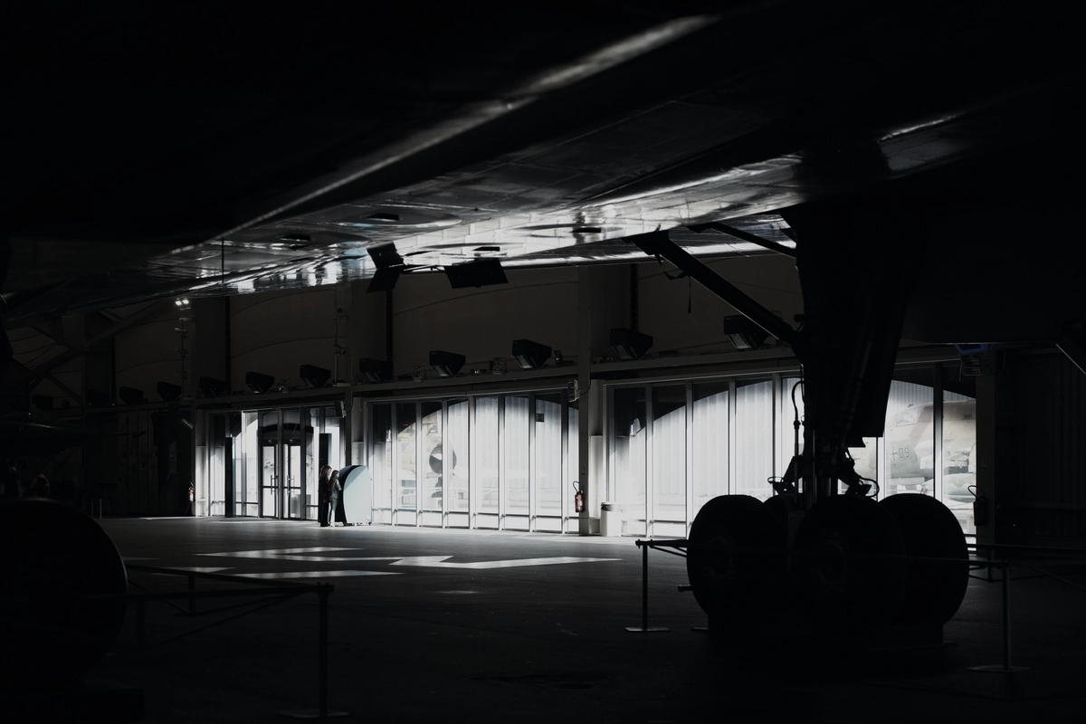 An aircraft's landing gear silhouetted inside a dimly lit maintenance hangar.