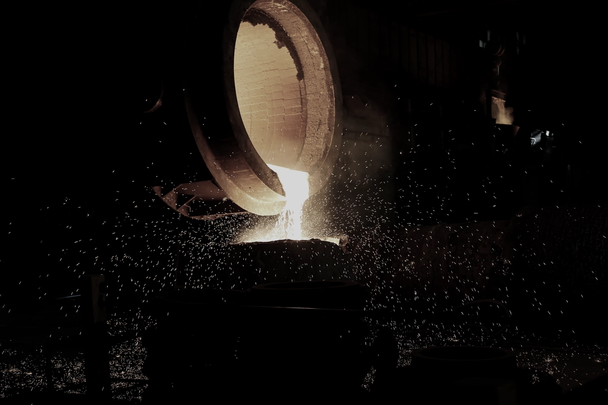 Molten metal pouring from a ladle in a dark foundry, throwing sparks.