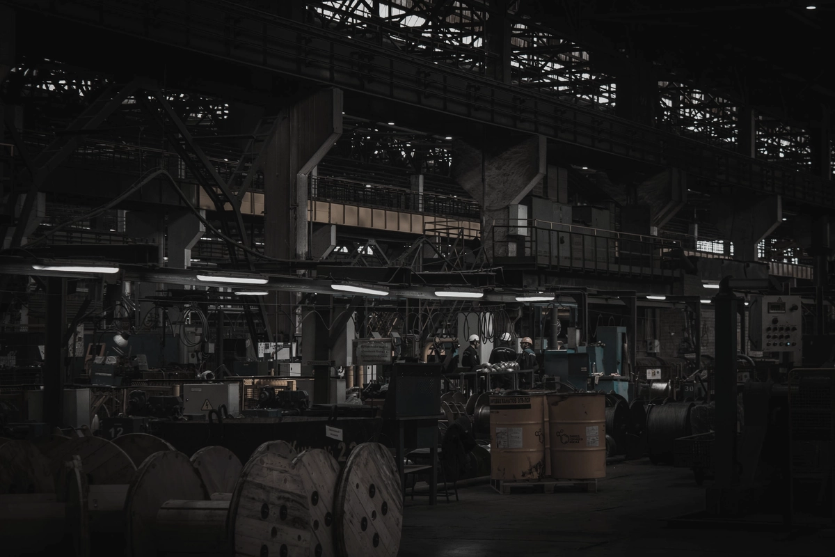 A wide, dimly lit production hall with machinery, gantries and cable spools.