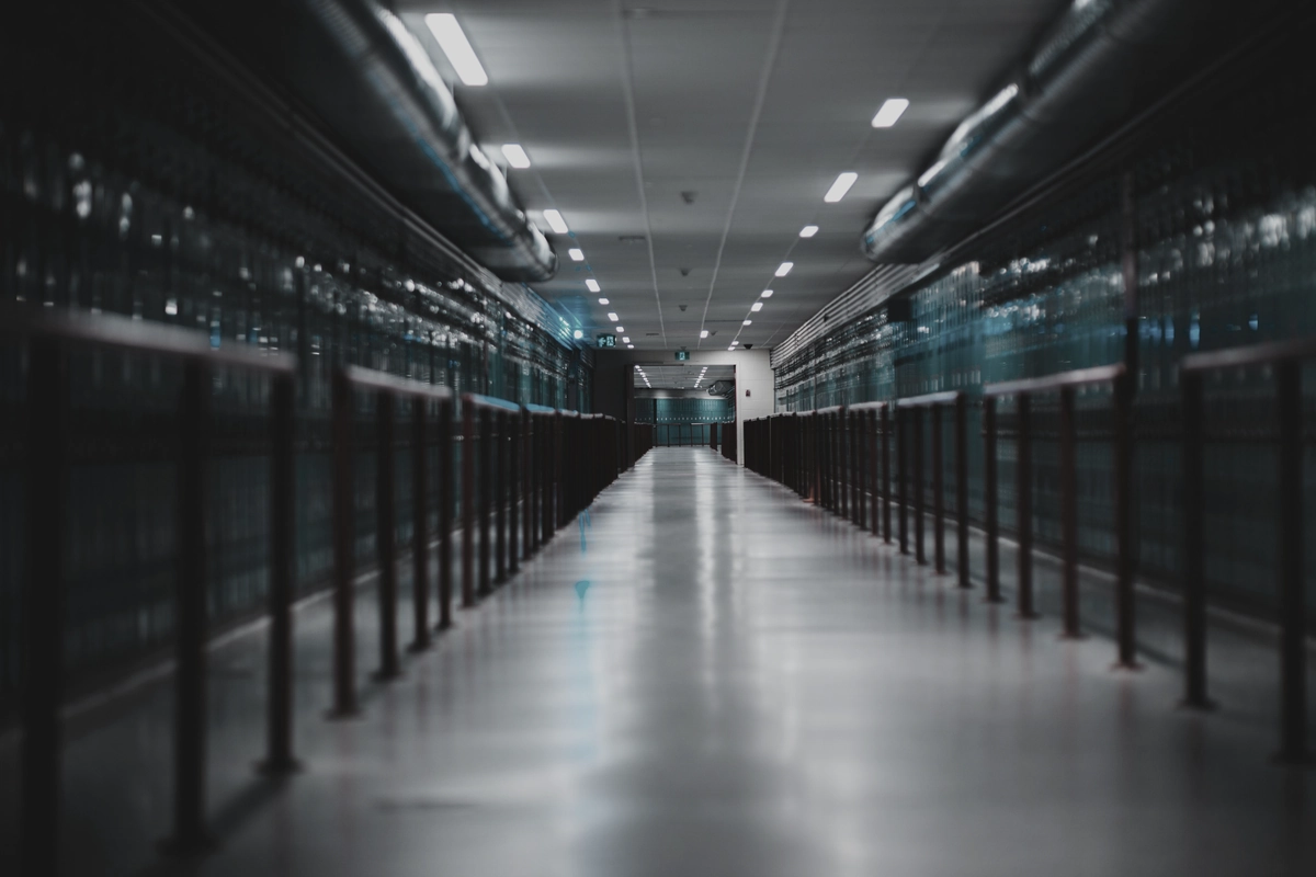 A long data-hall corridor between enclosed rows of racks, lit by cold overhead strips.